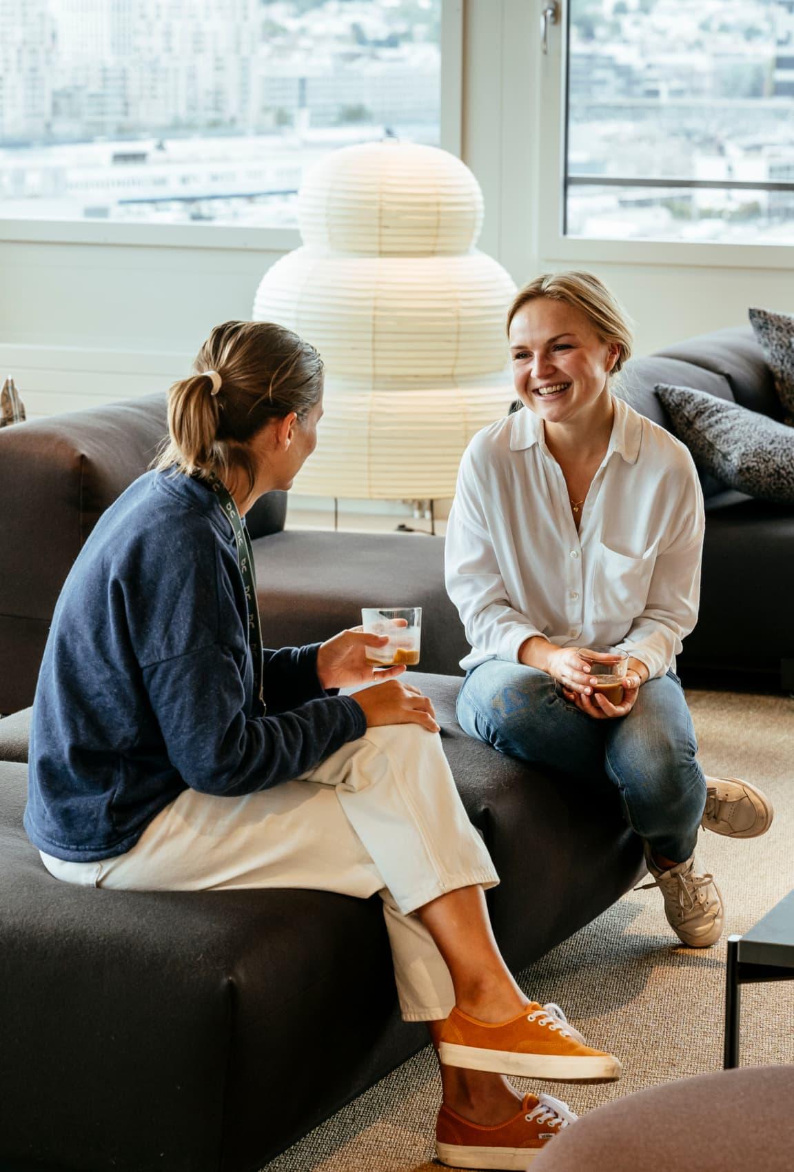 Two women having a conversation on a sofa whilst smiling.