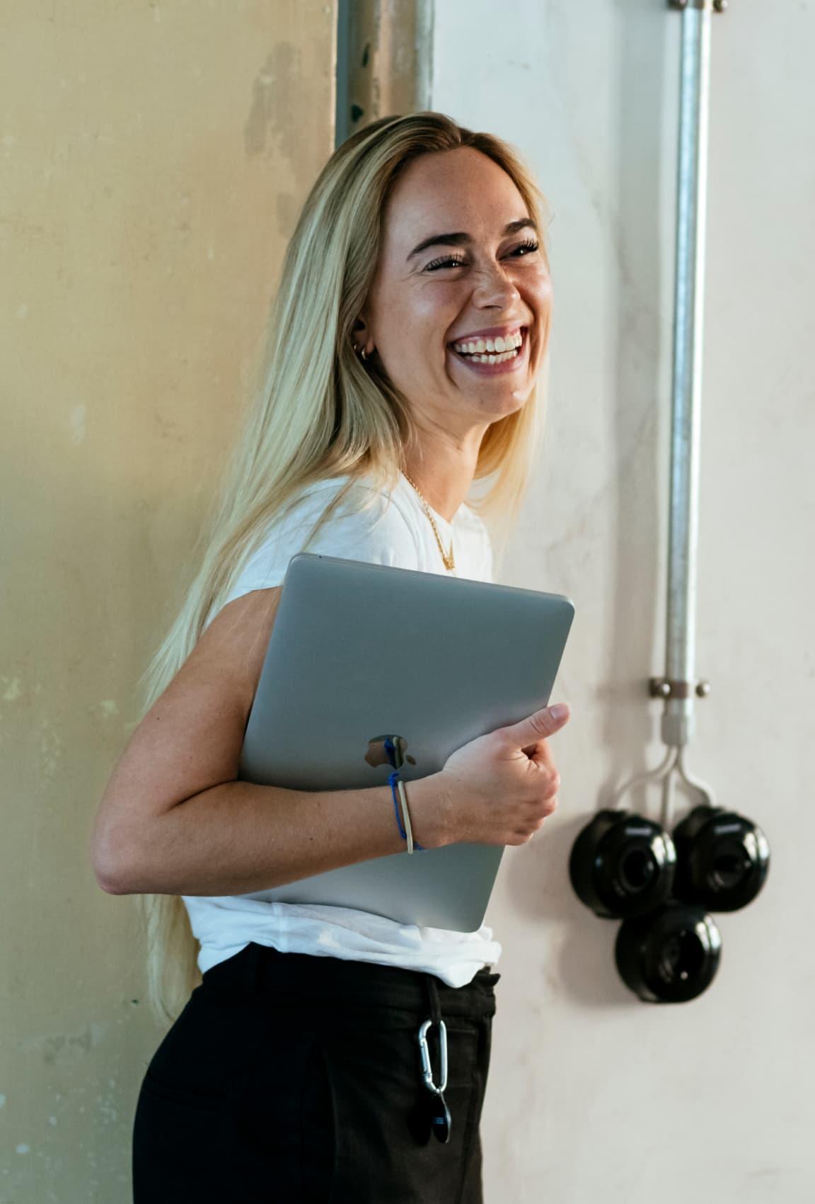 A woman smiling towards the camera holding her laptop