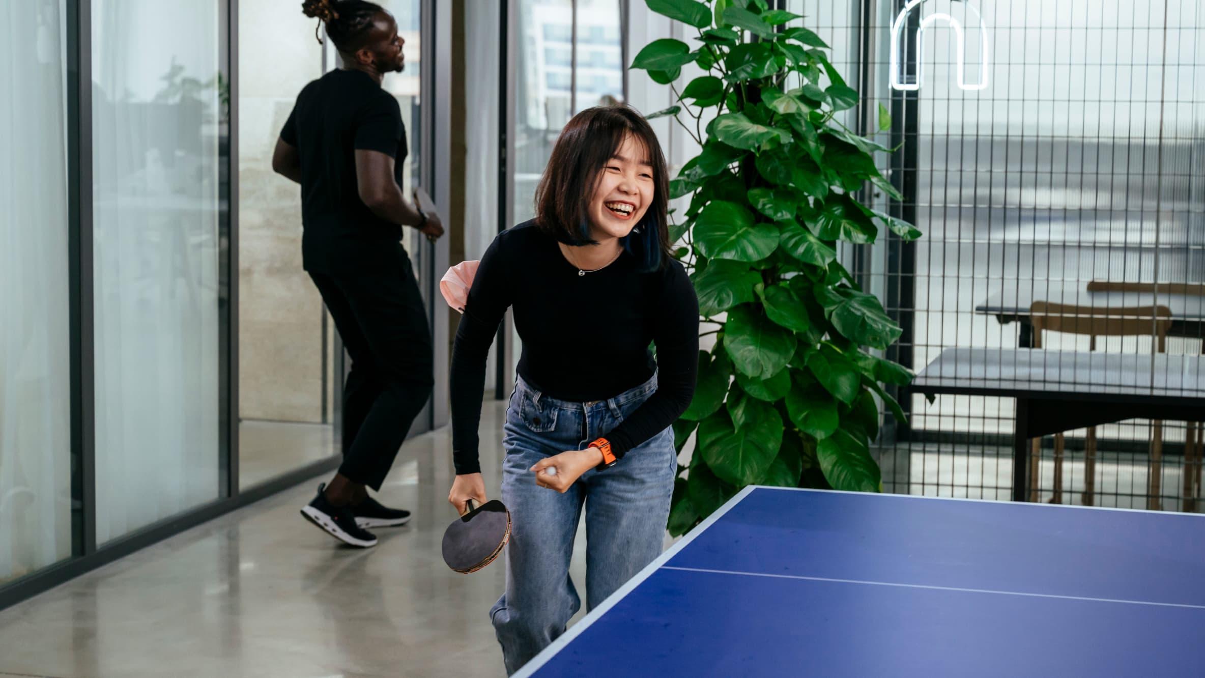 Woman laughing as she plays ping pong in the office!