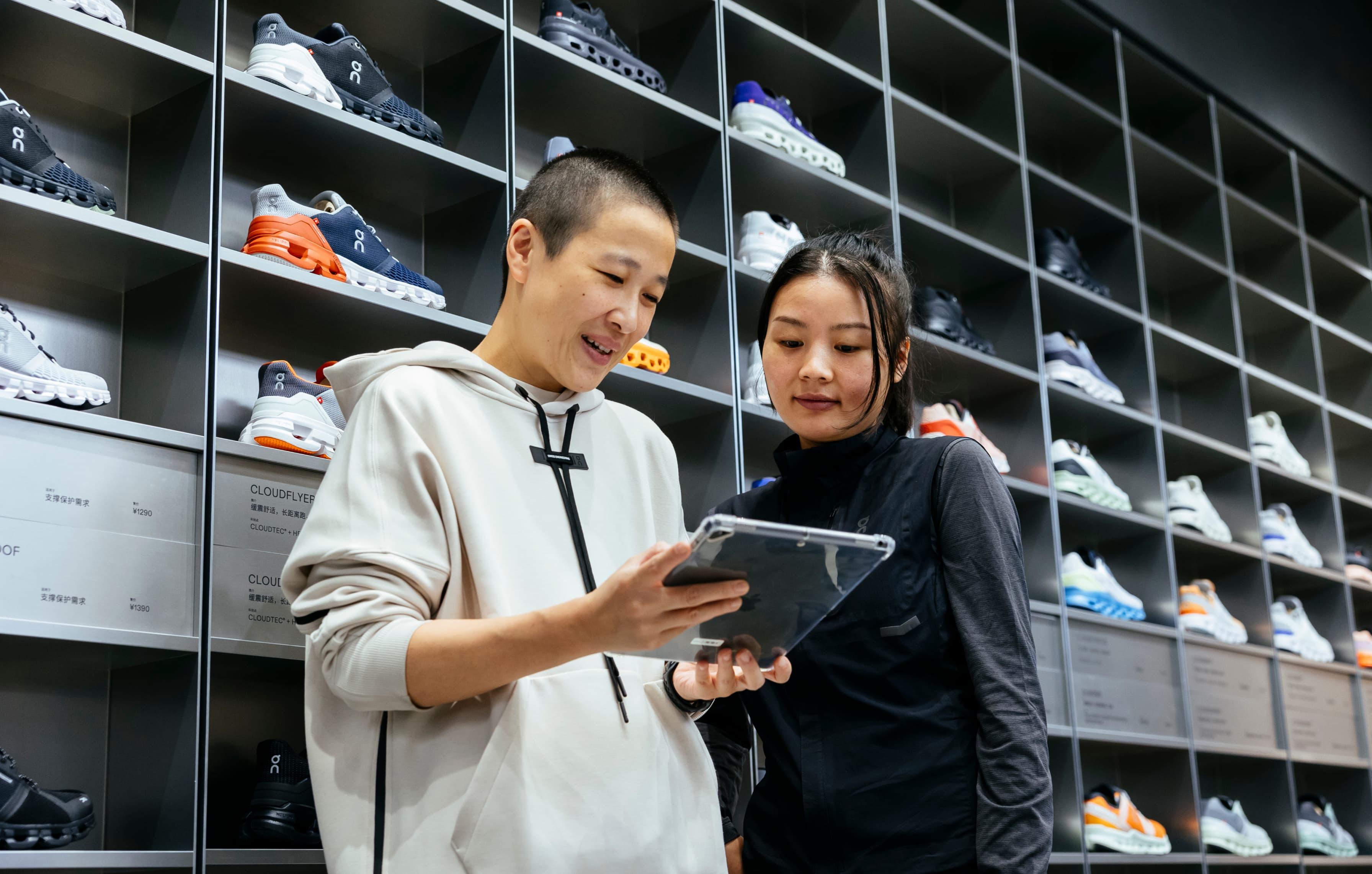 Two people looking at a laptop with rows of running shoes behind them