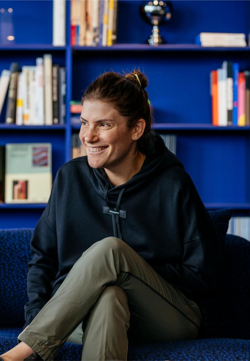 woman wearing onrunning hoody smiling in front of blue bookcase