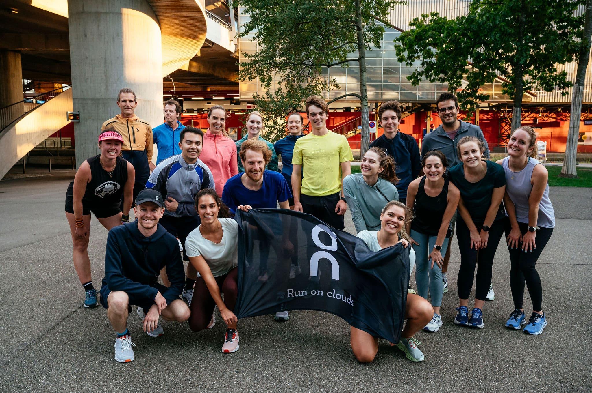 a large group of runners holding an On flag smiling at the camera 
