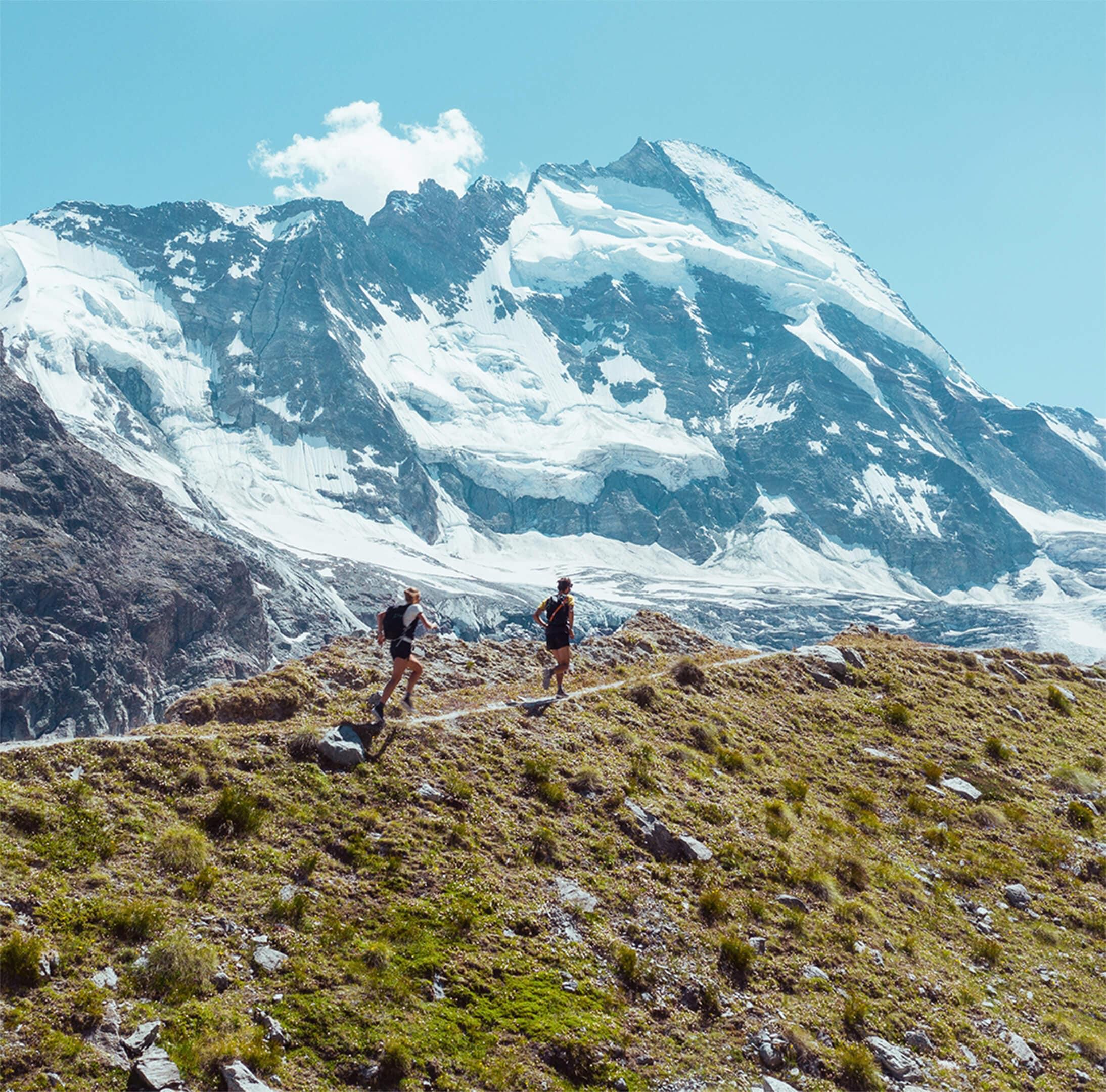 Two people jogging on a trail with a snowy mountain peak in the background